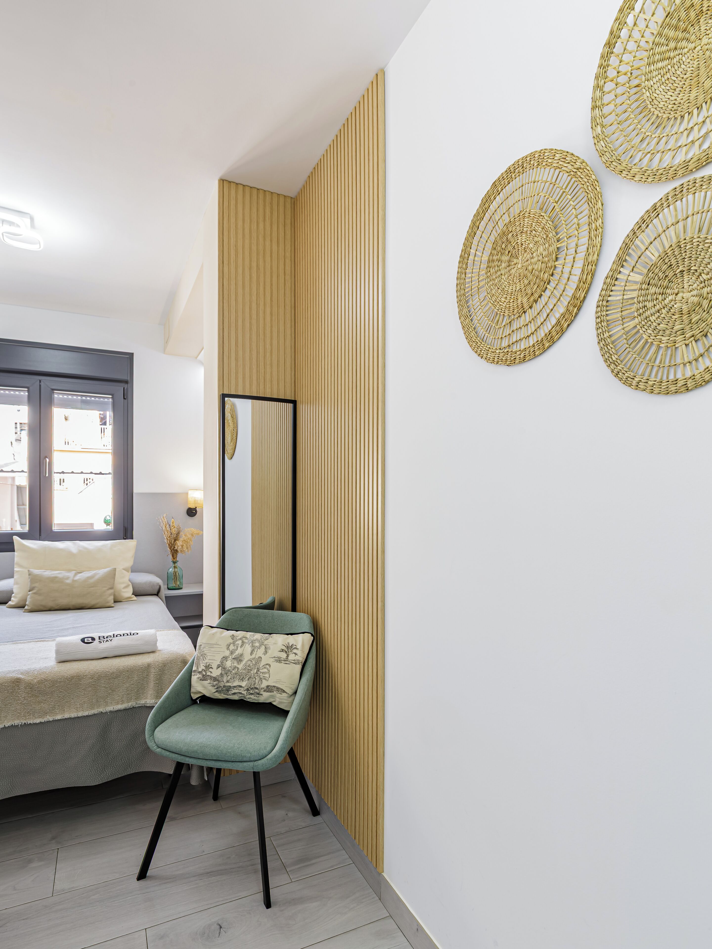 Un dormitorio moderno con cama, una silla, un espejo y decoración de arte tejido en la pared.