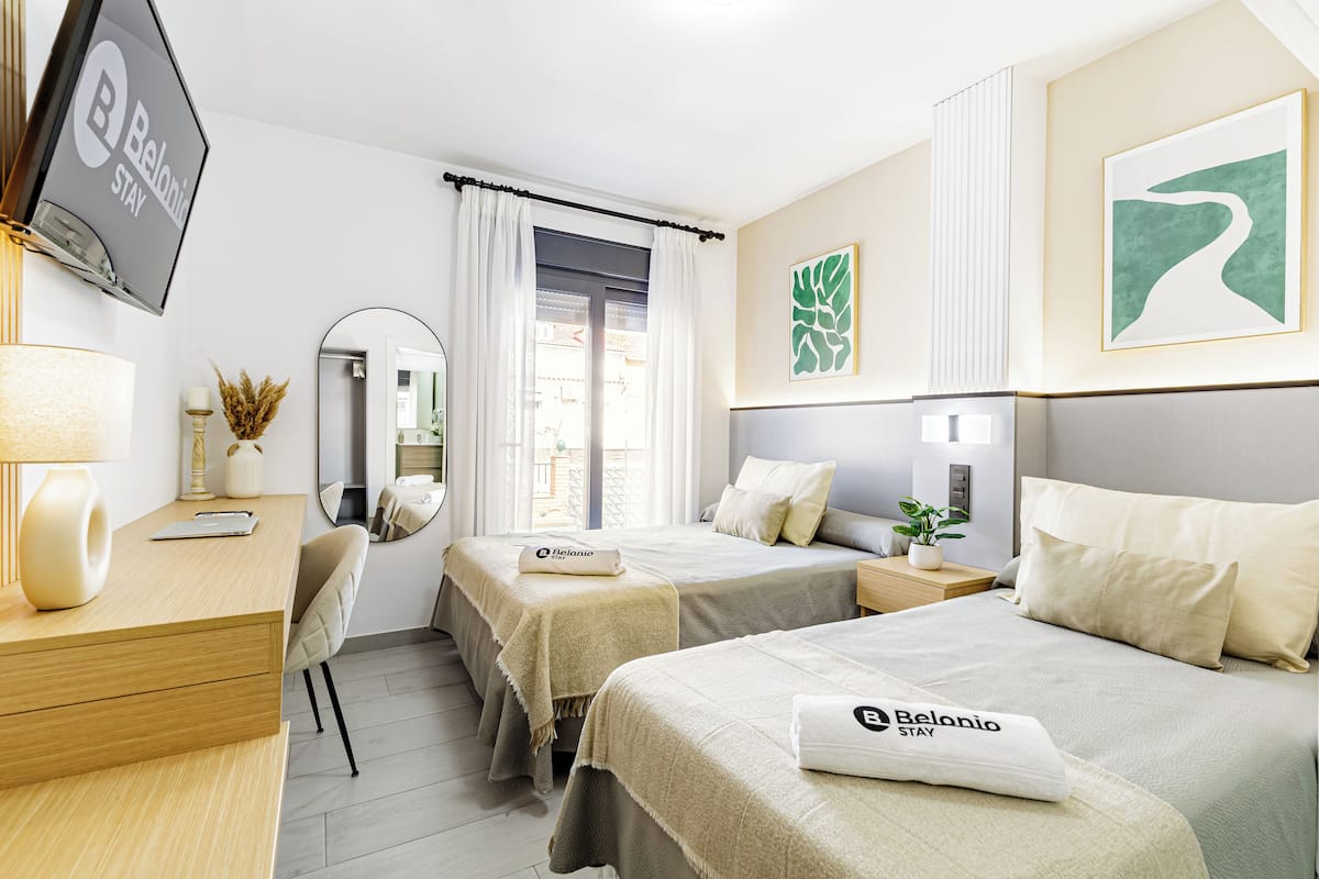 Ett hotellrum med två sängar, ett skrivbord, en stol, en TV, en spegel och konstverk på väggarna.