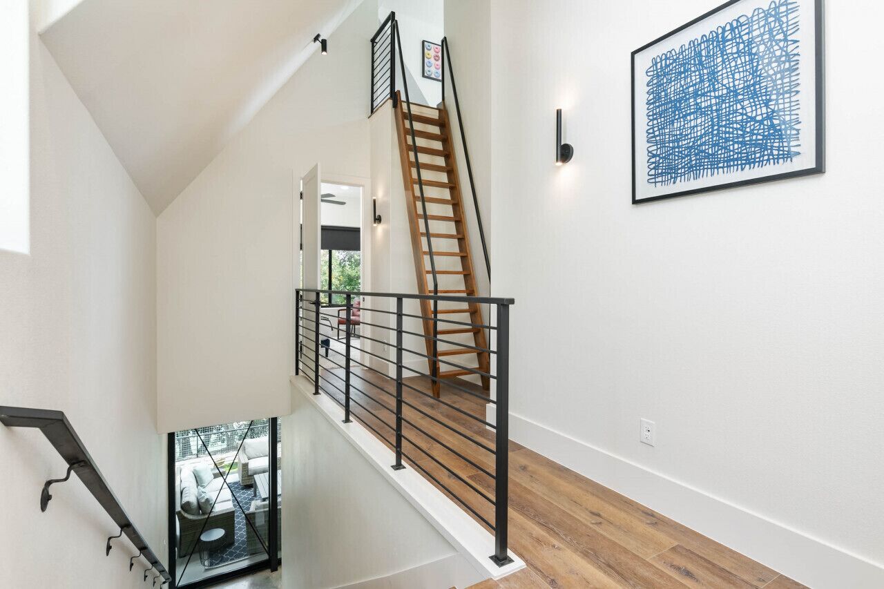 Una escalera moderna con barandilla de madera y pasamanos de metal negro, que conduce a un piso superior.