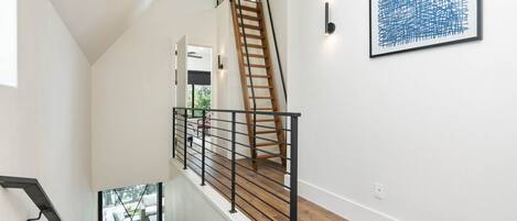 Una escalera moderna con barandilla de madera y pasamanos de metal negro, que conduce a un piso superior.