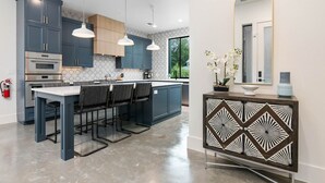 A modern kitchen with dark blue cabinets, stainless steel appliances, and a central island with bar stools.