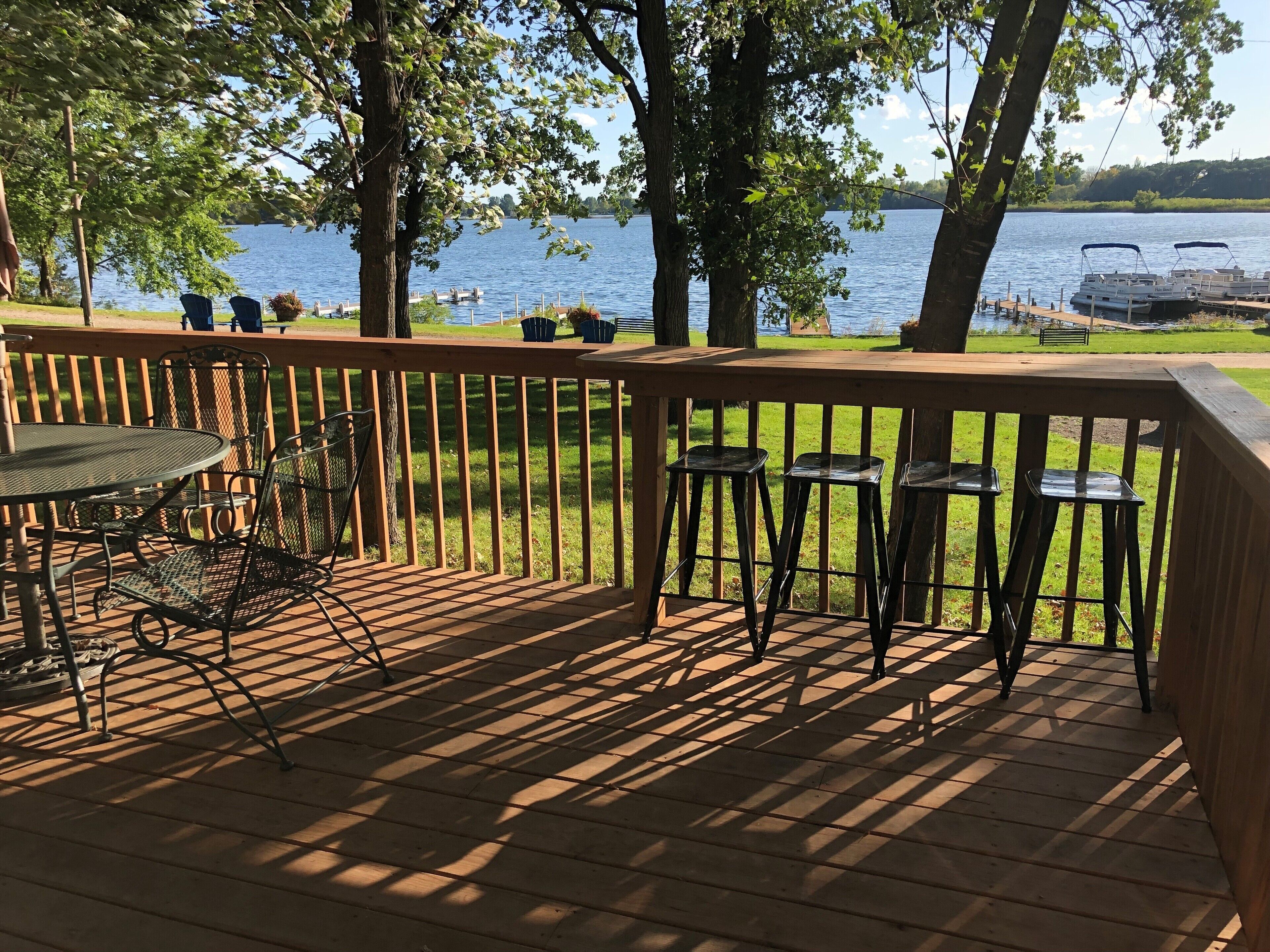 A wooden deck with a table and chairs, overlooking a lake with boats.
