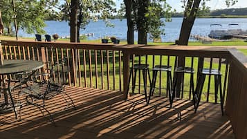 A wooden deck with a table and chairs, overlooking a lake with boats.
