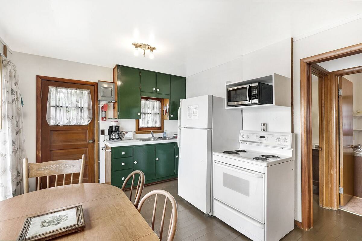 A compact kitchen with green cabinets, a white refrigerator, a microwave, a stove, and a dining table with chairs.