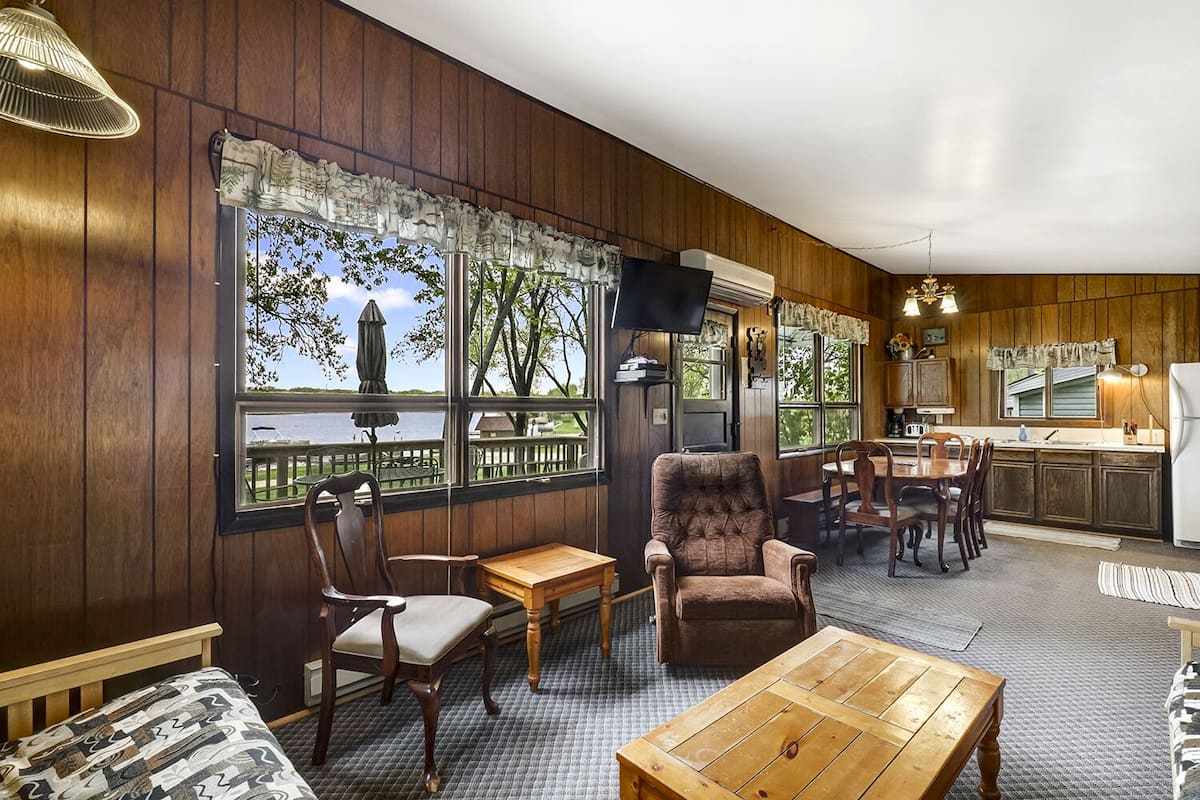 A cozy room with a wooden interior, a dining area with a table and chairs, and a view of the outdoors through large windows.