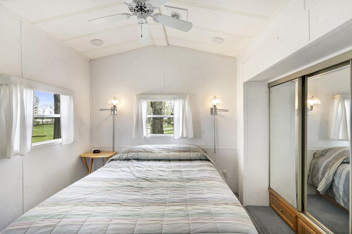 A bedroom with a bed, a nightstand, two wall-mounted lamps, a ceiling fan, and a large mirror.