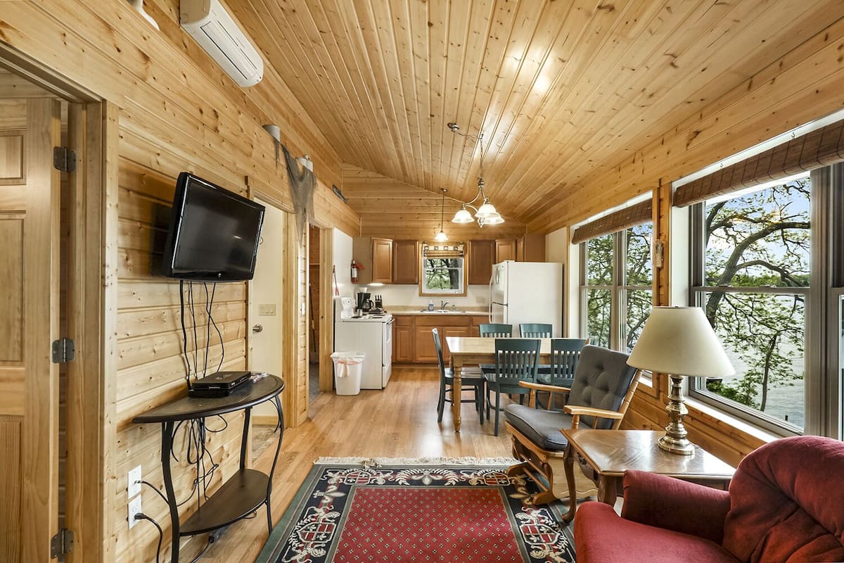 A wooden cabin interior with a dining area, kitchen, and a TV mounted on the wall.