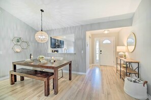 Un comedor con una mesa y banco de madera, una lámpara colgante y una cocina al fondo.