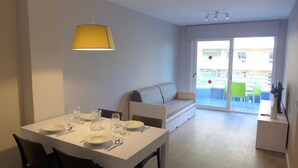 Ein moderner Essbereich mit einem weißen Tisch, gedeckt für vier Personen, einer gelben Pendelleuchte und einem grauen Sofa im Hintergrund.