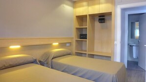 Ein Schlafzimmer mit zwei Betten, einem Holzschrank und einem durchgehenden Türspalt sichtbaren Badezimmer.