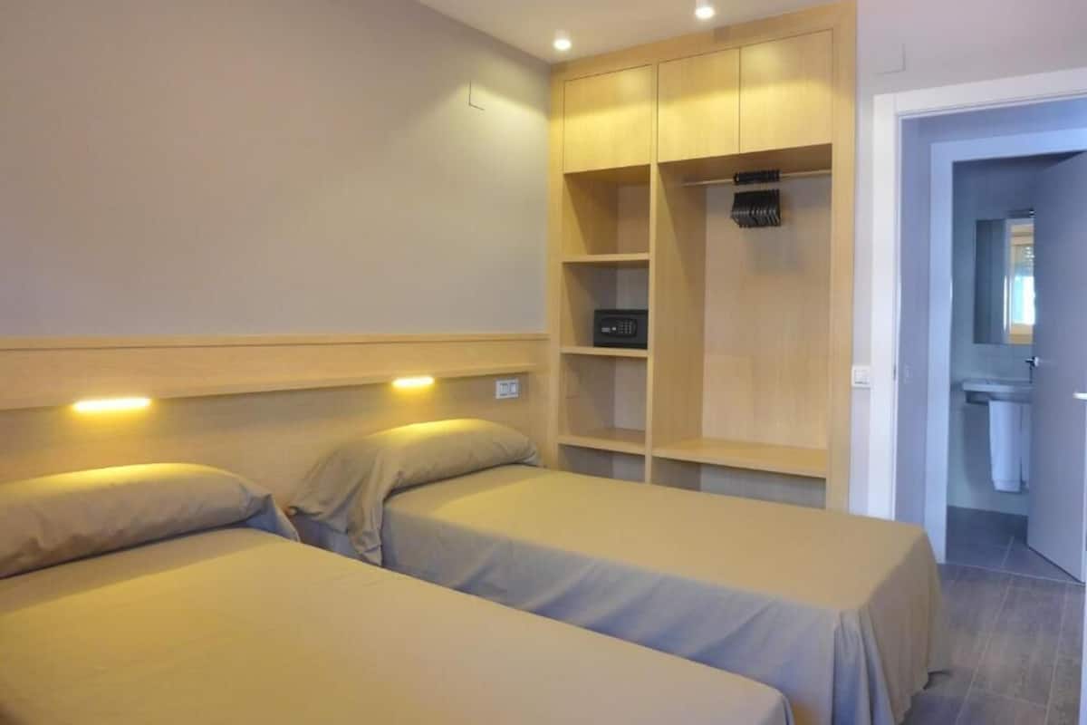 Une chambre avec deux lits, une armoire en bois et une salle de bain visible à travers une porte ouverte.