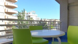 Ein Balkon mit einem runden Tisch und vier grünen Stühlen, mit Blick auf eine Stadtlandschaft mit Gebäuden und einem Hotelschild.