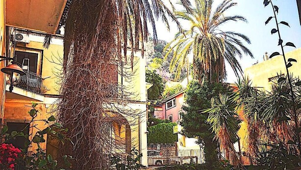 Une rue étroite, bordée de bâtiments des deux côtés, dont certains sont ornés de balcons et de plantes grimpantes.