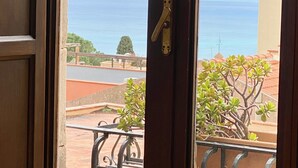 Vue depuis un balcon doté d’une balustrade en métal, donnant sur une zone côtière, avec un ciel dégagé et la mer à l’horizon.