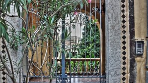 Un portail en fer forgé orné d’un motif décoratif, un mur en pierre et une plaque métallique.