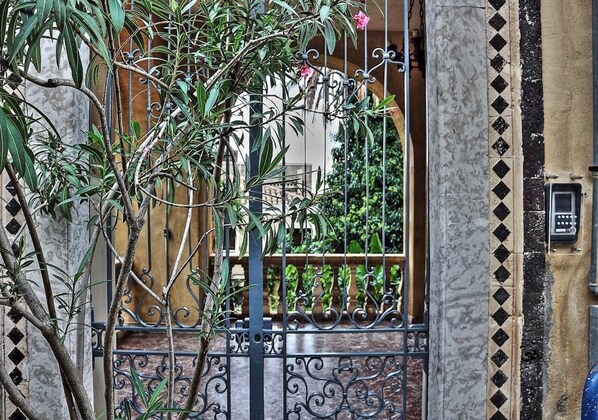 A wrought iron gate with a decorative pattern, a stone wall, and a metal plaque.