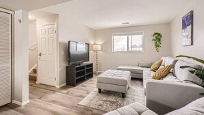 A living room with a flat-screen TV, a grey sofa, an ottoman, and a small coffee table. - Centrally located for adventures (Westminster)