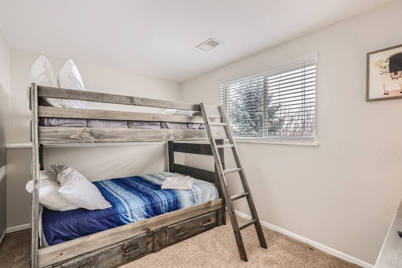 A bunk bed with a ladder, white walls, a window with blinds, and a framed picture on the wall.