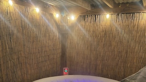 Un bain à remous doté d’un panneau de commande, entouré de murs en bambou et surmonté d’un sol à motifs.