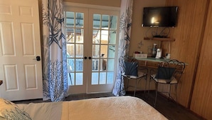 Une chambre à coucher comprenant un lit, un bureau, une chaise, un téléviseur et une porte donnant sur l’extérieur.