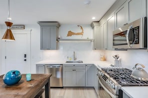 Una cocina moderna con armarios grises, electrodomésticos de acero inoxidable, una mesa de madera y un adorno en la pared.
