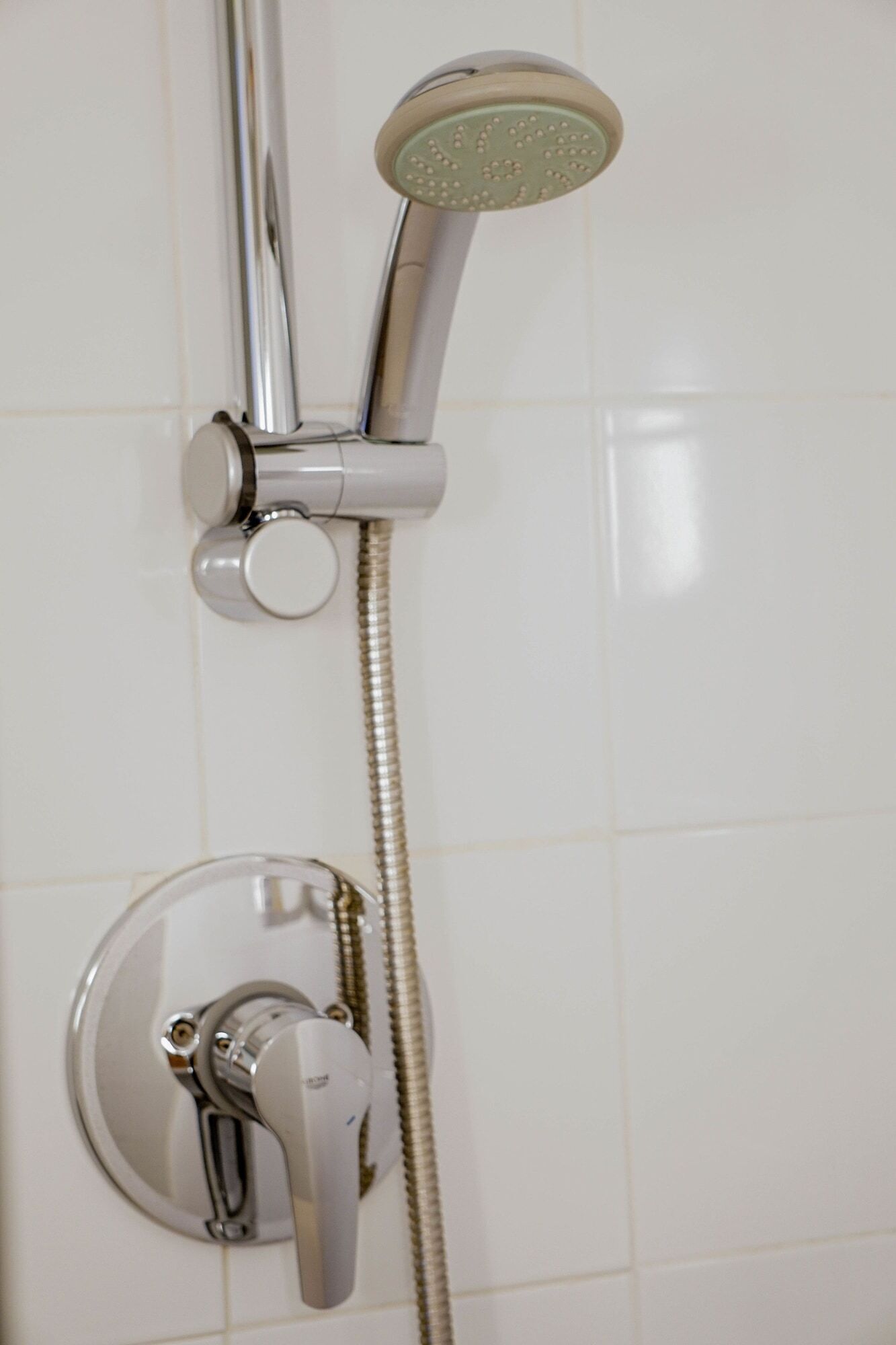 Een douche met een handdouche en een bedieningskraan aan de muur.