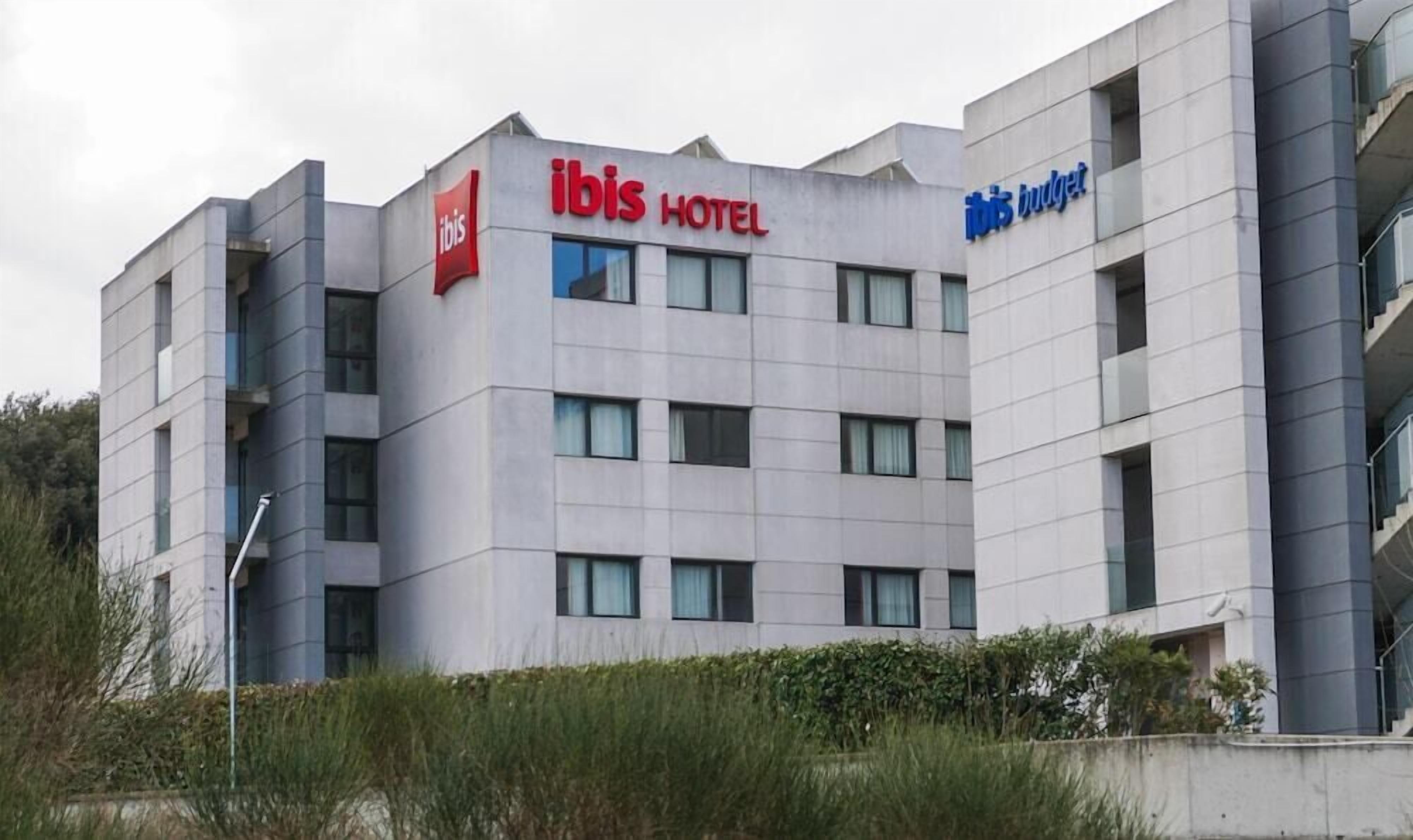 A modern hotel building with multiple floors, featuring the ibis logo and the ibis budget logo.