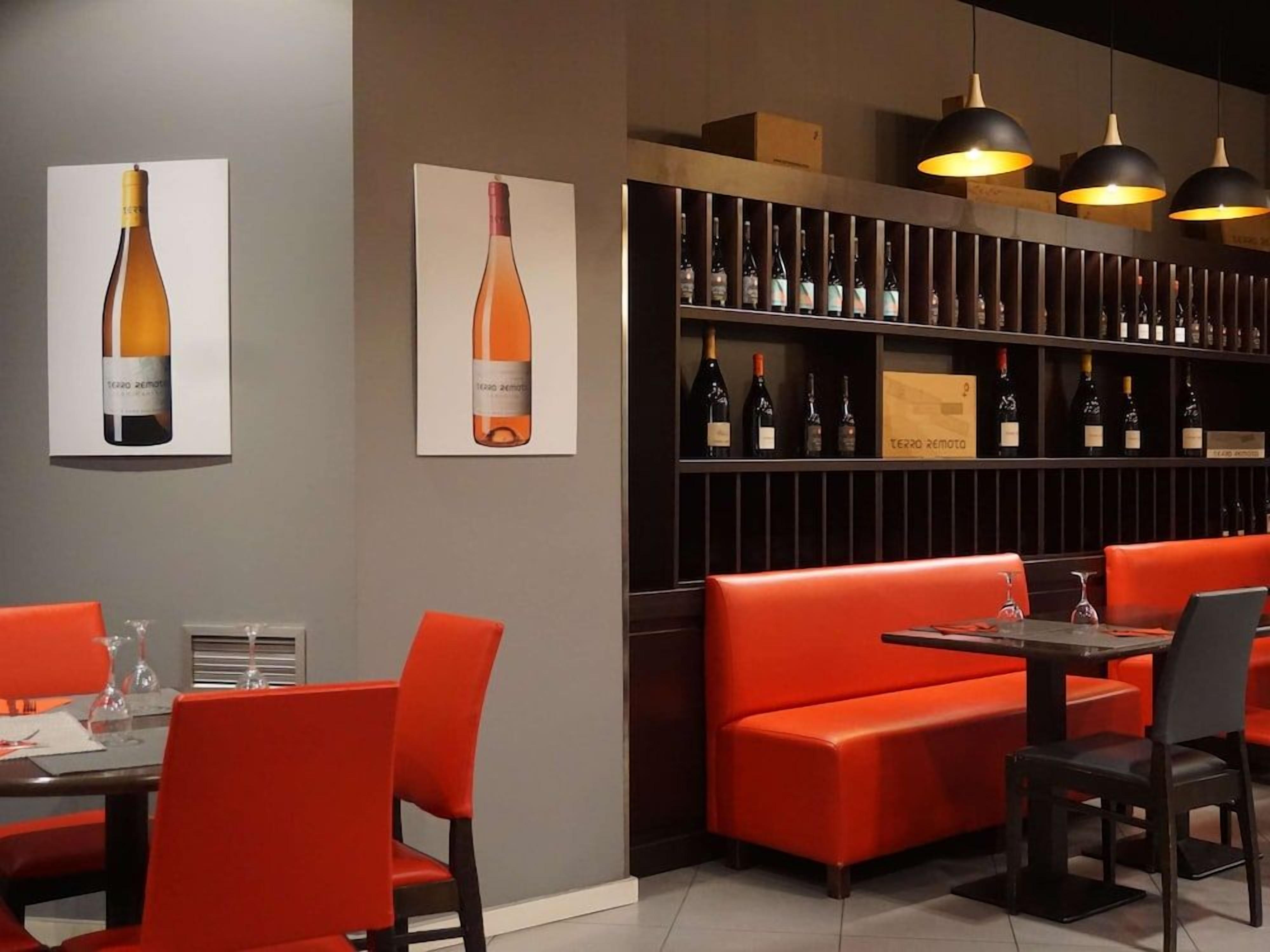 Een restaurantinterieur met rode zitplaatsen, een wijnrek en hanglampen.