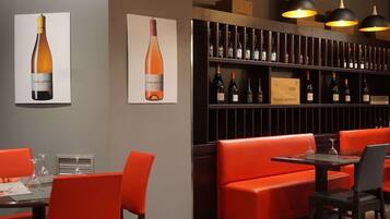 Een restaurantinterieur met rode zitplaatsen, een wijnrek en hanglampen.