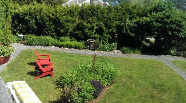 A well-maintained garden with a red chair, a small tree, and a variety of plants. - New, top deck couples retreat overlooking Southwest harbor! (Southwest Harbor)