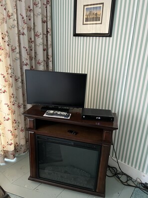 A television on a wooden stand with a remote control, a DVD player, and a picture frame on the wall.