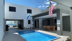 A modern building with a swimming pool, outdoor seating, and flags.