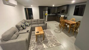 A modern living room with a grey sectional sofa, a wooden coffee table, and a dining area with a wooden table and chairs.