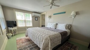 Un dormitorio con cama, ventilador de techo, televisión y ventana con persianas.