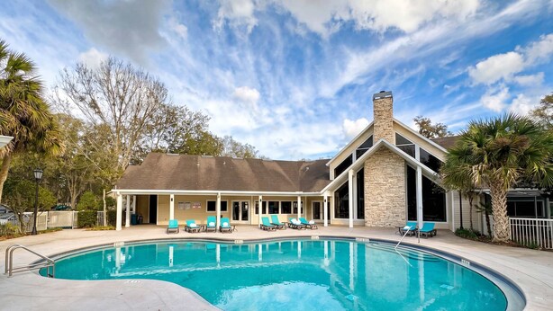 A swimming pool with lounge chairs, a covered patio, and a stone chimney. - The Nomad at Gables | King Bed • Pool • Garage (Gainesville)