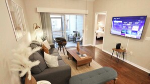 A modern living room with a grey sofa, a coffee table, and a flat-screen TV mounted on the wall. - The Nomad at Gables | King Bed • Pool • Garage (Gainesville)