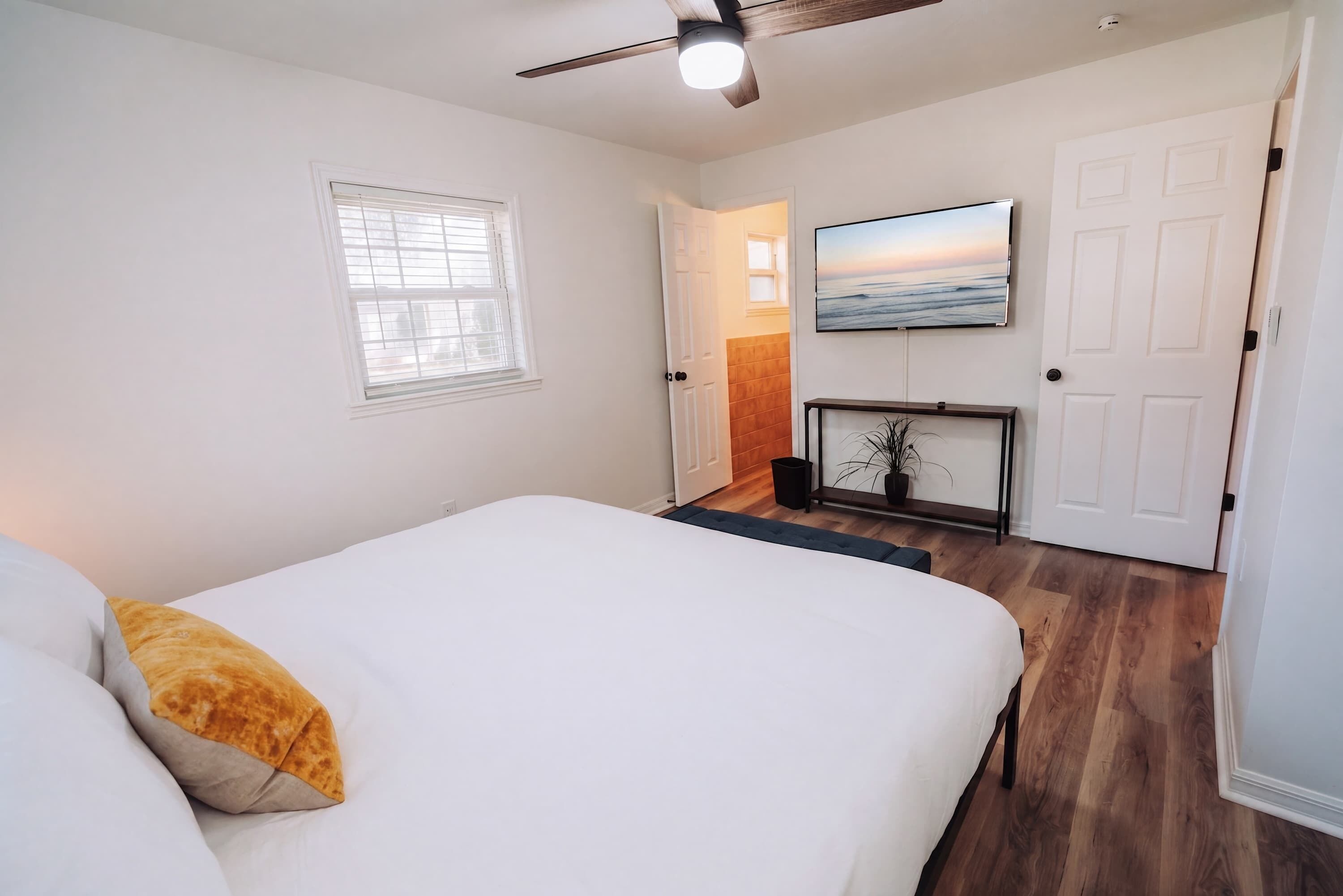 A bedroom with a bed, a ceiling fan, a TV, and a door leading to another room.