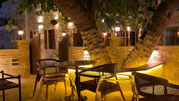 An outdoor dining area with stone walls, wooden furniture, and illuminated signs. - Dionysos 1789 Boutique Hotel (Foça)