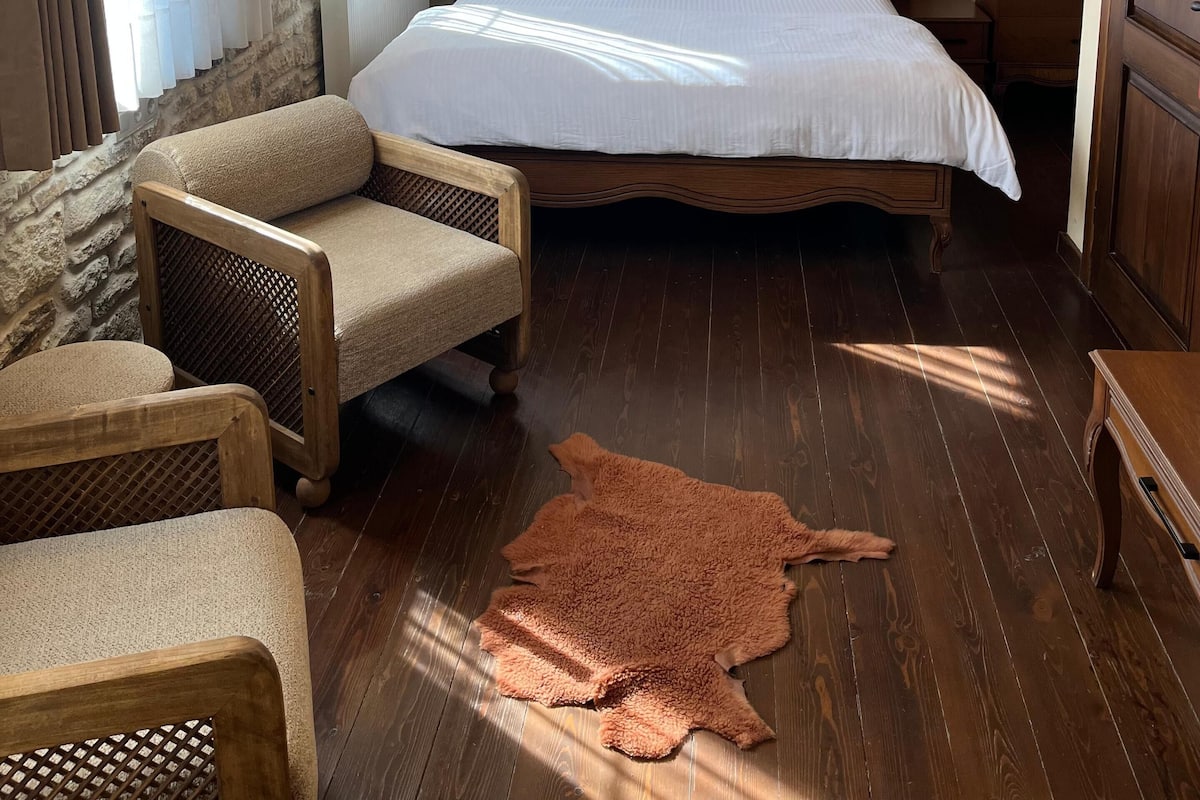 Quarto com cama de madeira, duas luminárias de apoio, um candelabro e parede de pedra.