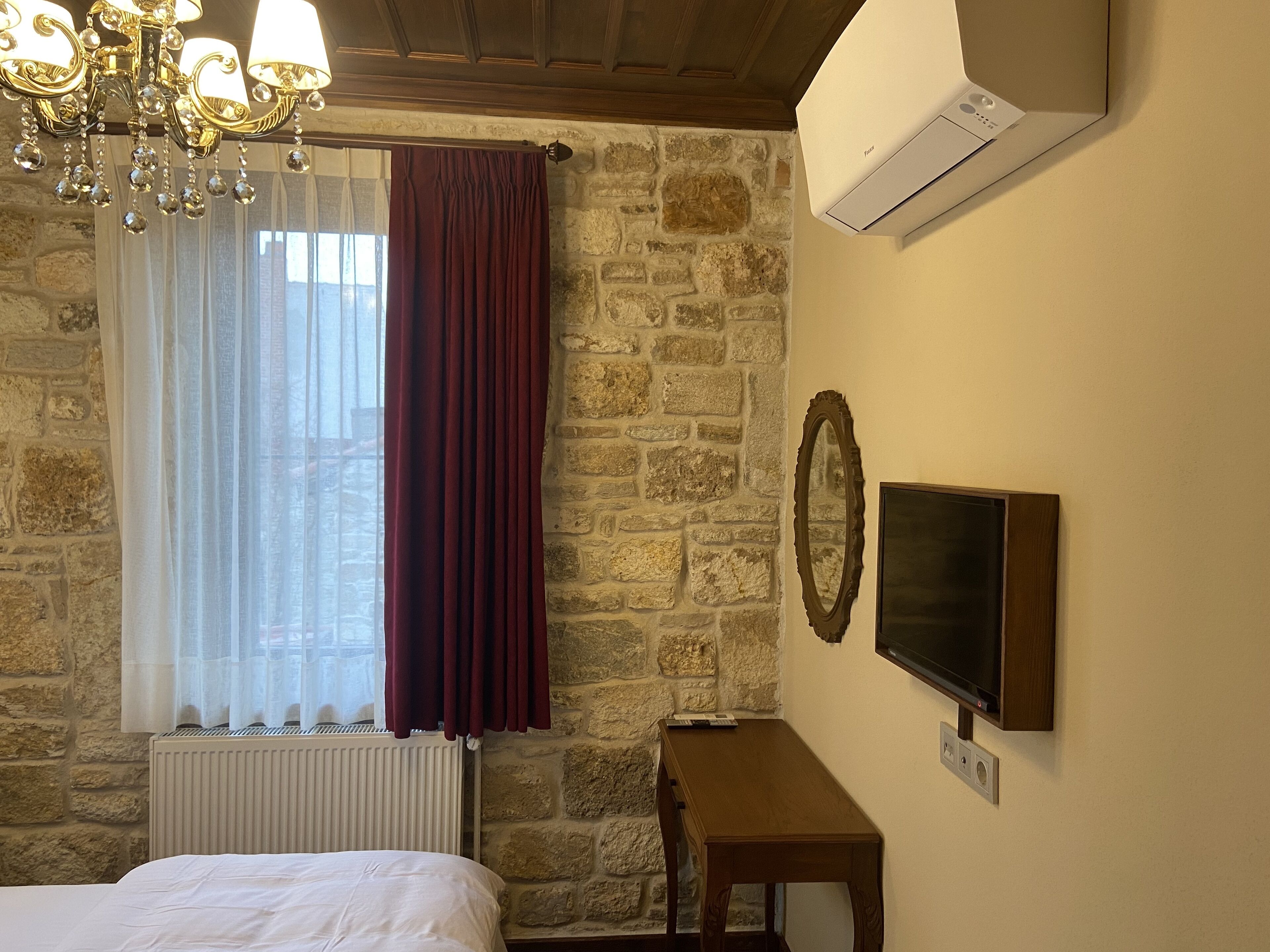 A room with a stone wall, a bed, a TV, and an air conditioner.
