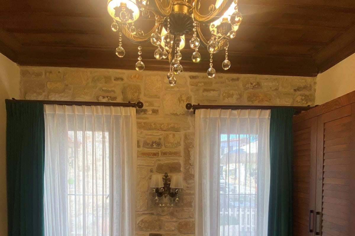 Quarto com uma cama grande, duas janelas com cortinas, um candelabro e uma parede de pedra.