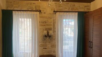 Un dormitorio con una cama grande, dos ventanas con cortinas, una araña y una pared de piedra.