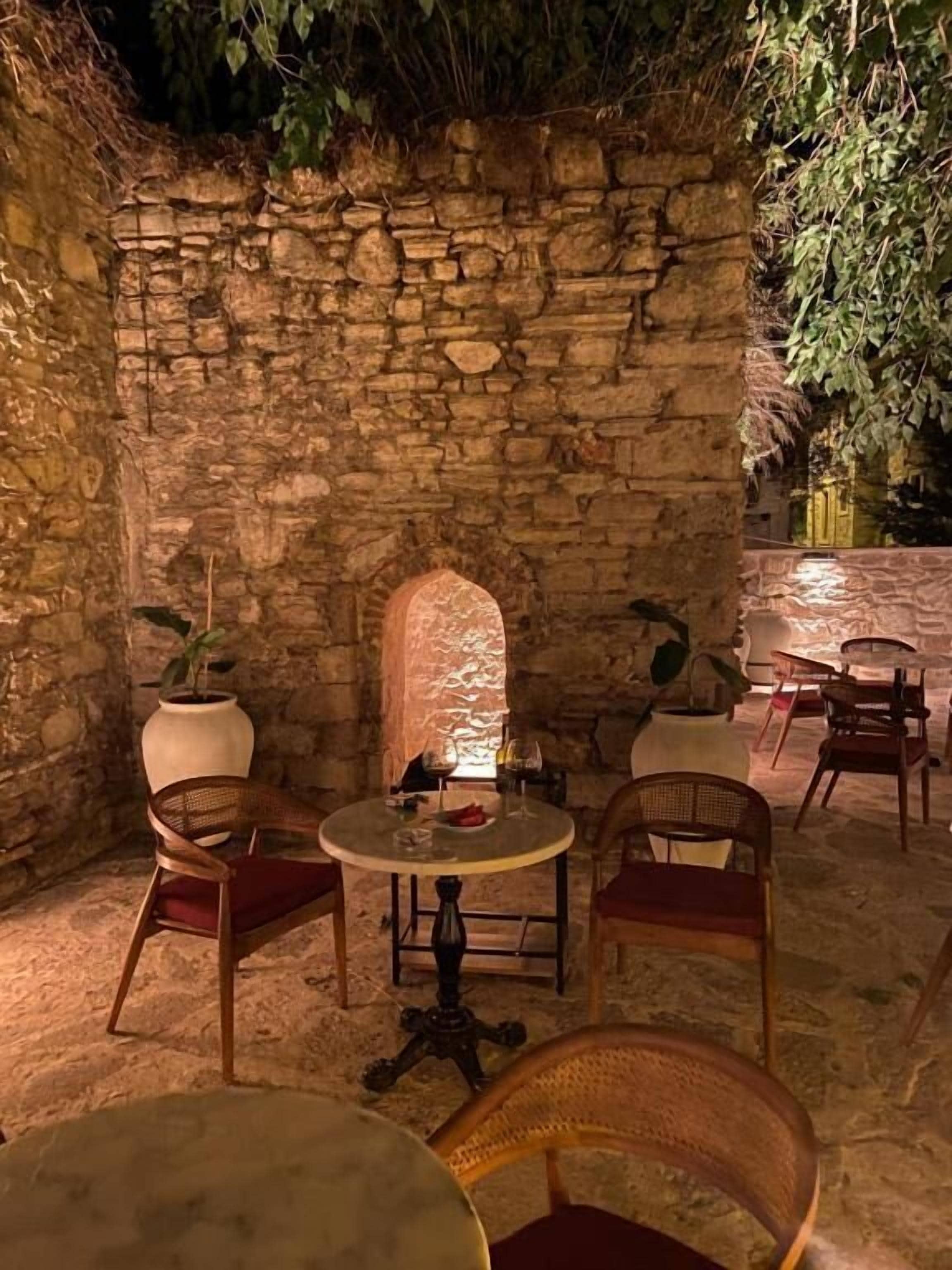 Un espacio al aire libre con paredes de piedra, mesas redondas y sillas de mimbre.