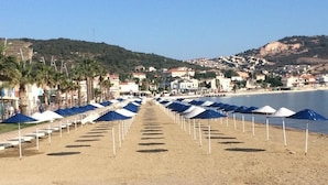 A beach with rows of umbrellas and a clear view of the sea and hills in the background. - Dionysos 1789 Boutique Hotel (Foça)