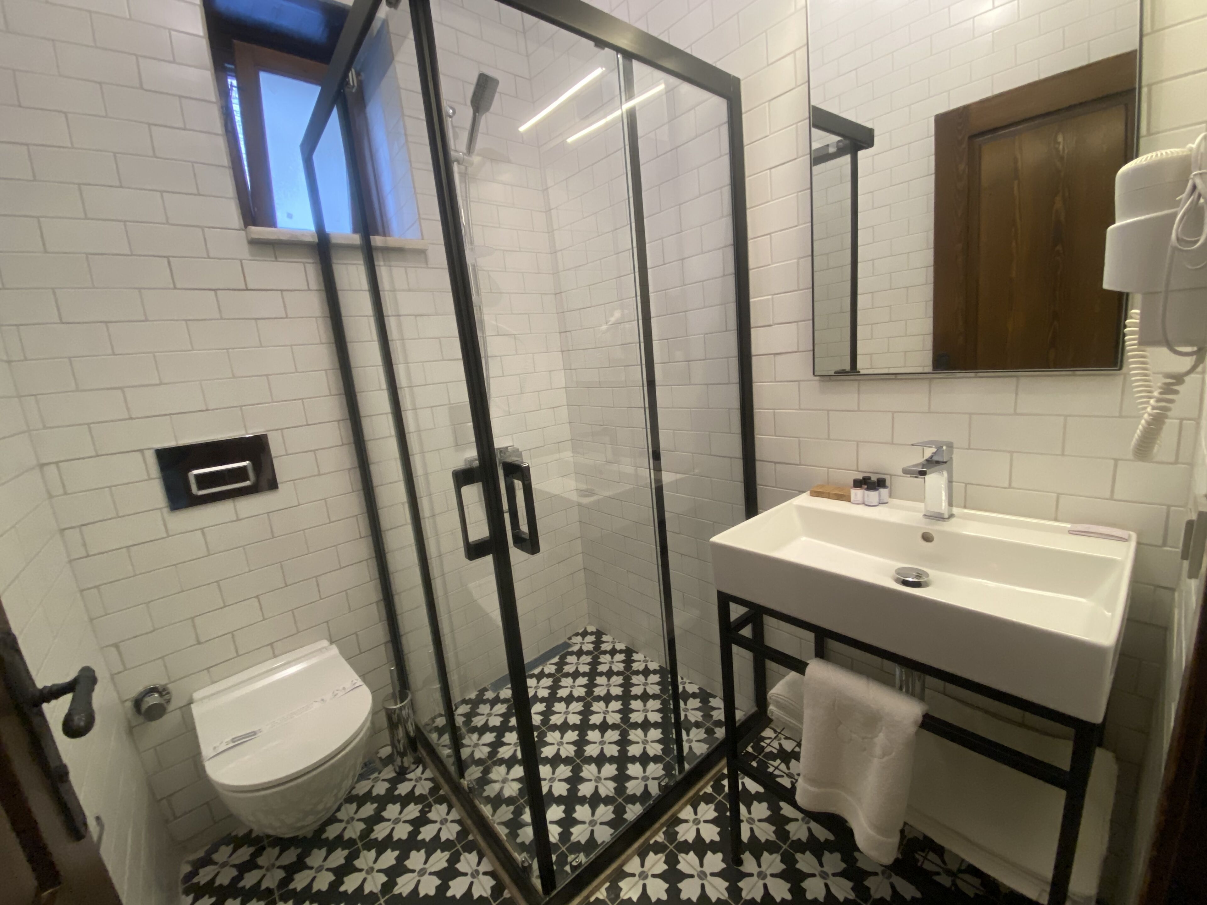 Een badkamer met een douche met glazen wand, een witte wastafel met spiegel erboven en een toilet.