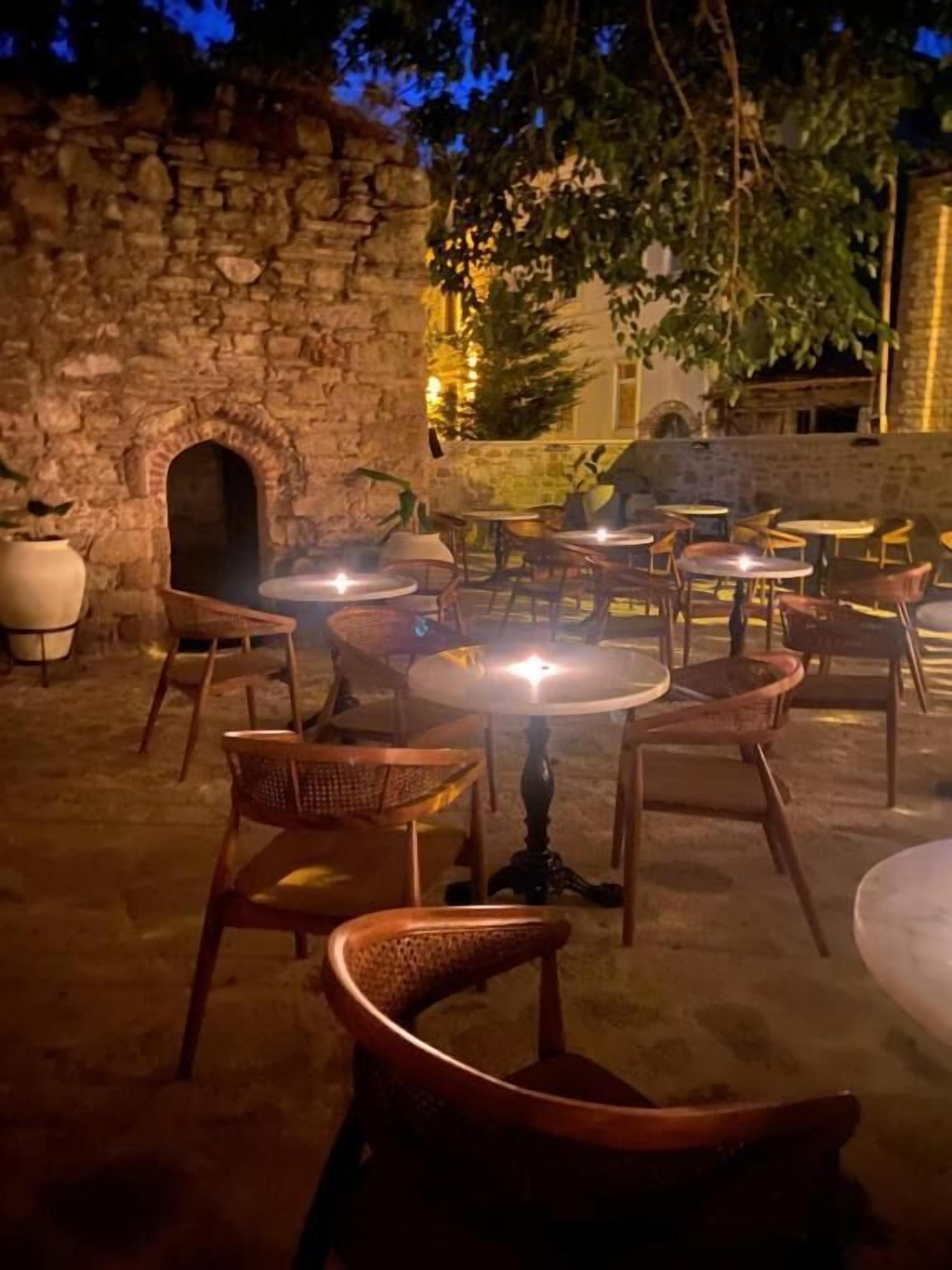 An outdoor seating area with wicker chairs and round tables, stone walls, and a brick oven.