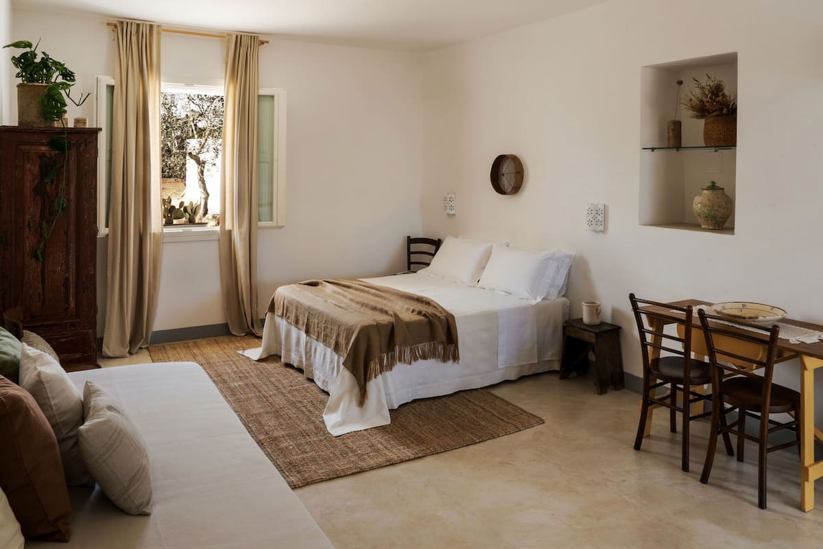 A bedroom with a bed, bedside table, chair, and a small table with a bowl.