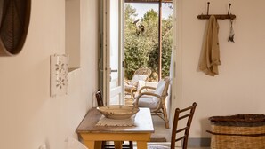 Una habitación con una cama, una mesa con sillas, una cesta de mimbre y vistas al exterior.