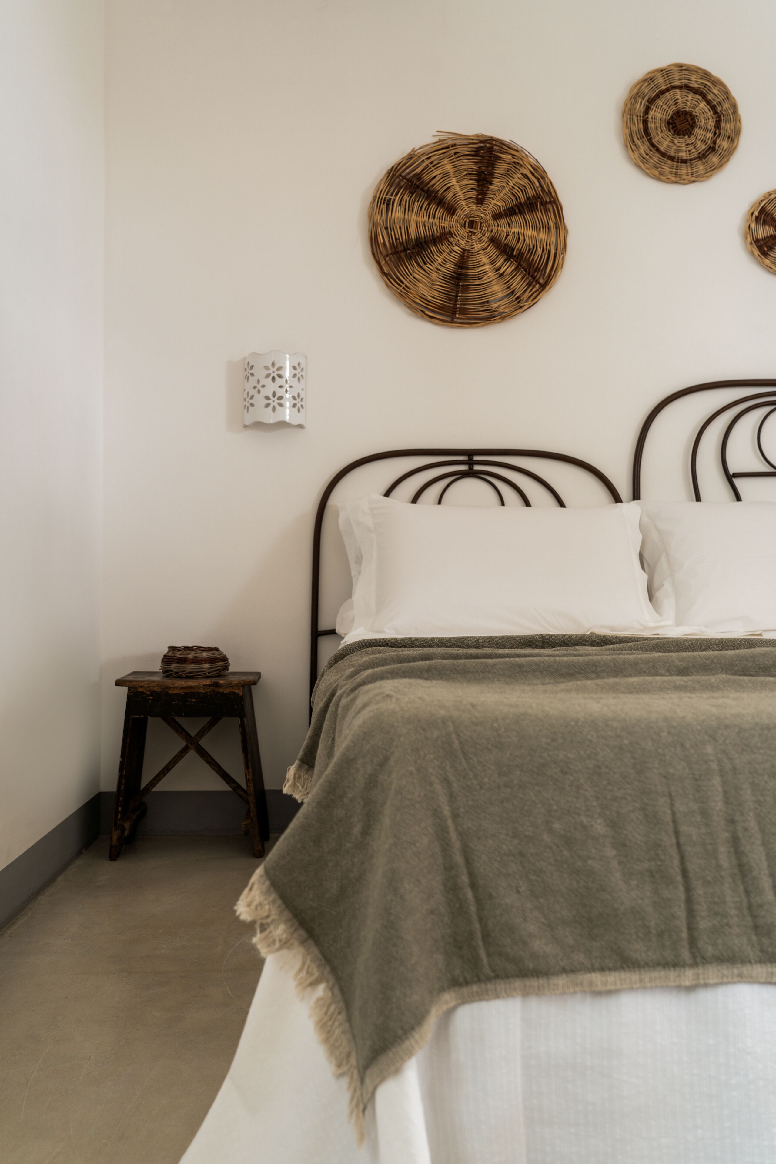 Quarto com uma cama, uma pequena mesa de cabeceira de madeira e três decorações de parede feitas em tecido.