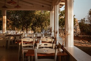 Un espace de restauration en plein air, avec des tables et des chaises, entouré d’arbres et d’un mur en pierre.